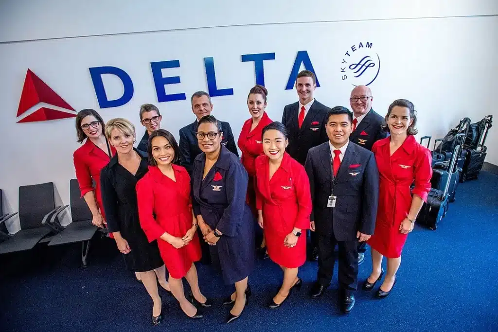 "Delta Air Lines SkyTeam flight attendants and pilots in uniform posing in front of Delta logo."